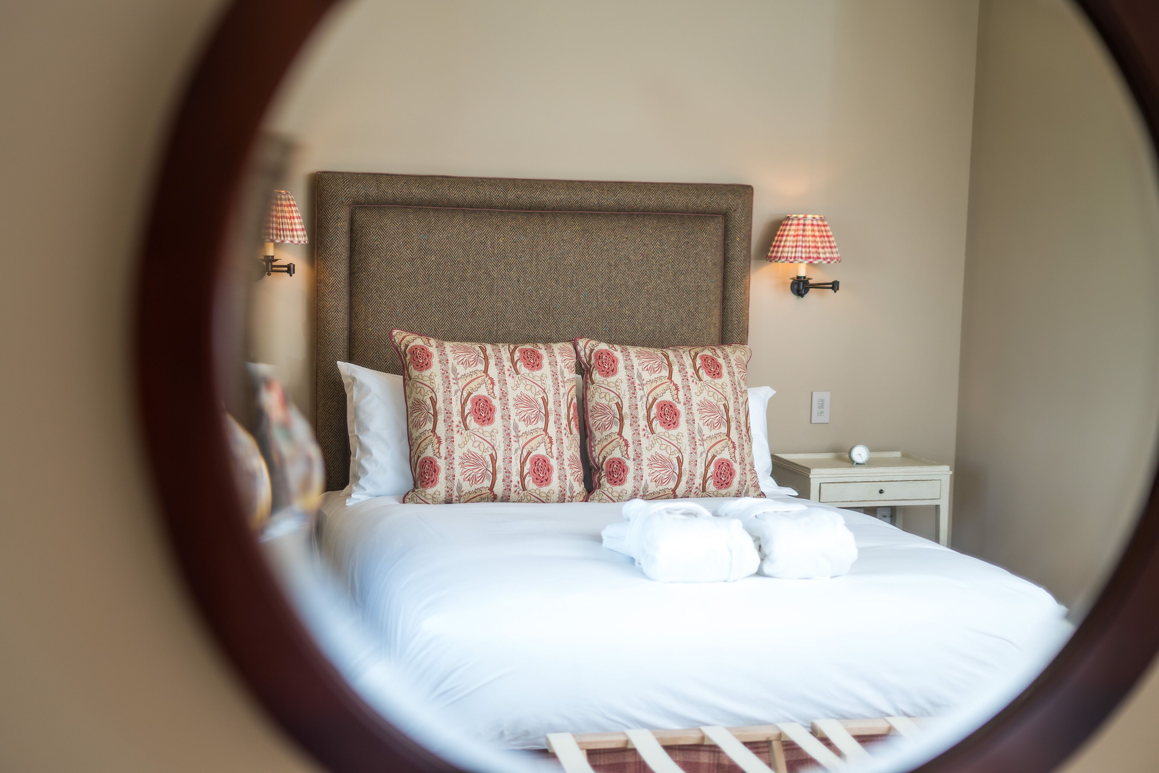 A neatly made bed with white linens and patterned pillows, a wooden headboard, and bedside lamps with checkered lampshades.