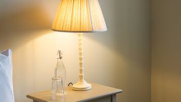A neatly made bed with a white pillow, a bedside table with a lamp, and two framed botanical prints on the wall.