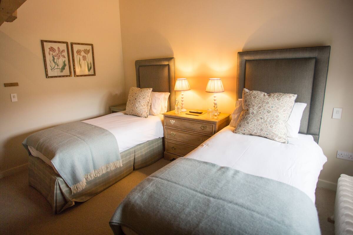 A hotel room with two single beds, a nightstand with lamps, and a small dresser.