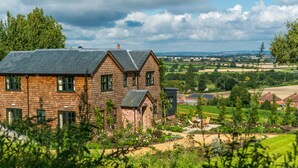 A two-story wooden house with a sloped roof, surrounded by a well-maintained garden and a view of the countryside. - The Three Daggers (Westbury)