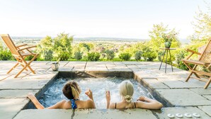 Two people relaxing in a hot tub with a scenic view of a garden and countryside. - The Three Daggers (Westbury)