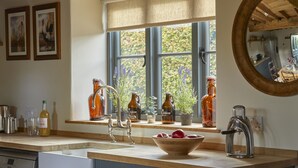 A kitchen with a wooden countertop, a sink, a window with blue shutters, and a mirror on the wall. - The Three Daggers (Westbury)