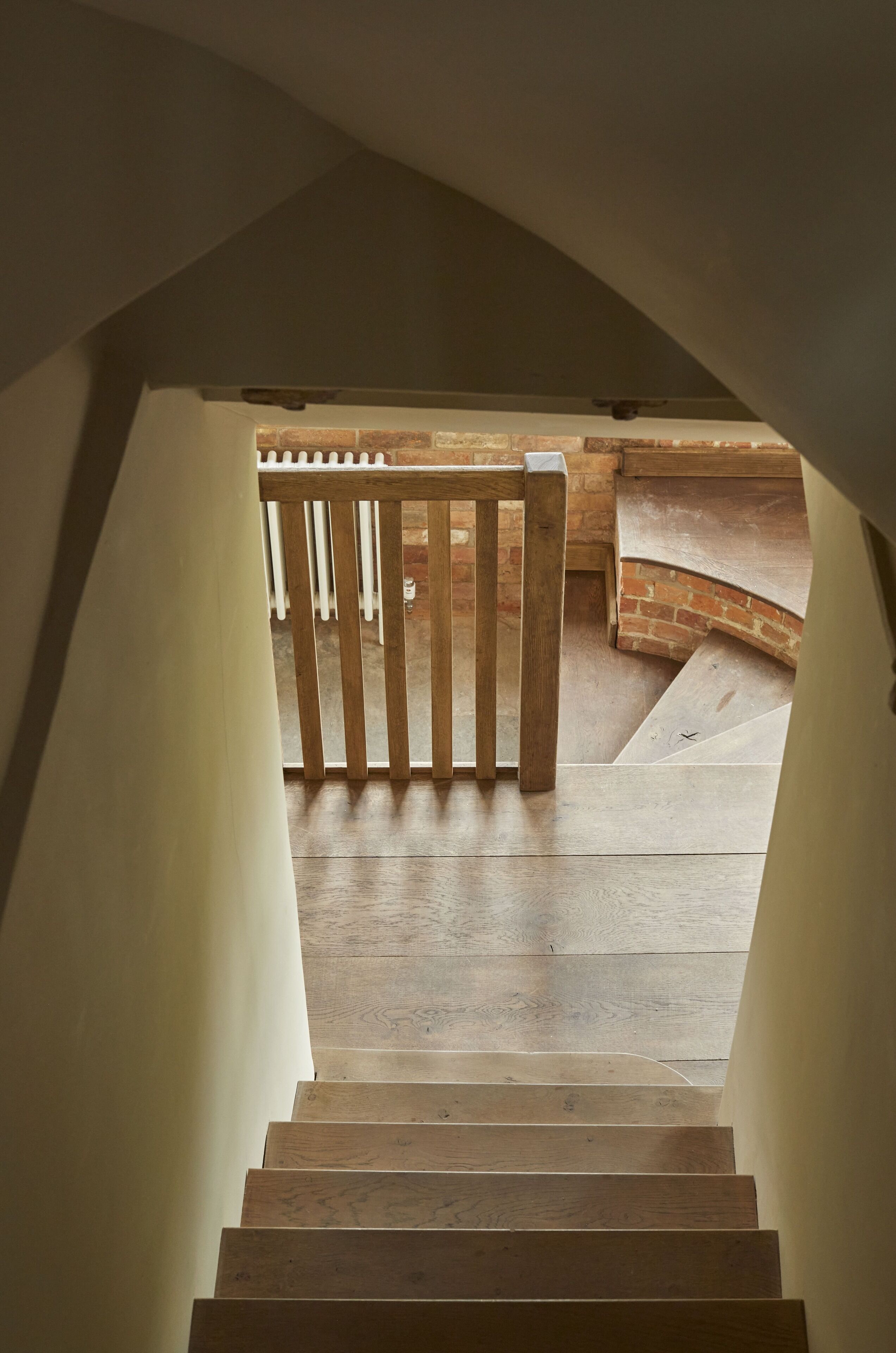 Un escalier en bois mène à un espace extérieur agrémenté d’un mur en briques et d’une clôture blanche.