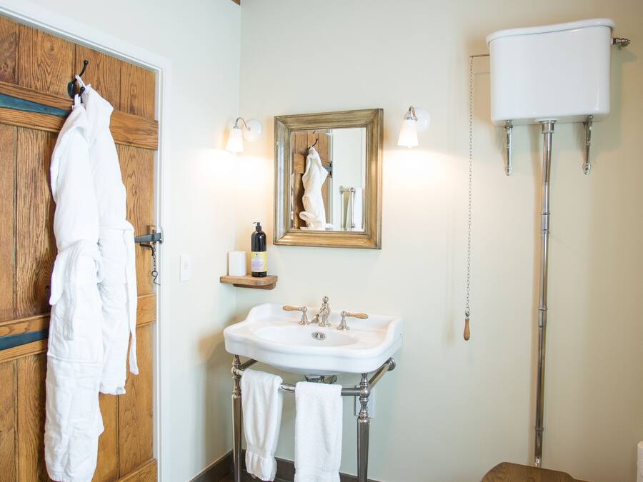 Un baño con puerta de madera, un lavabo blanco con espejo, un inodoro y un tapete de madera.