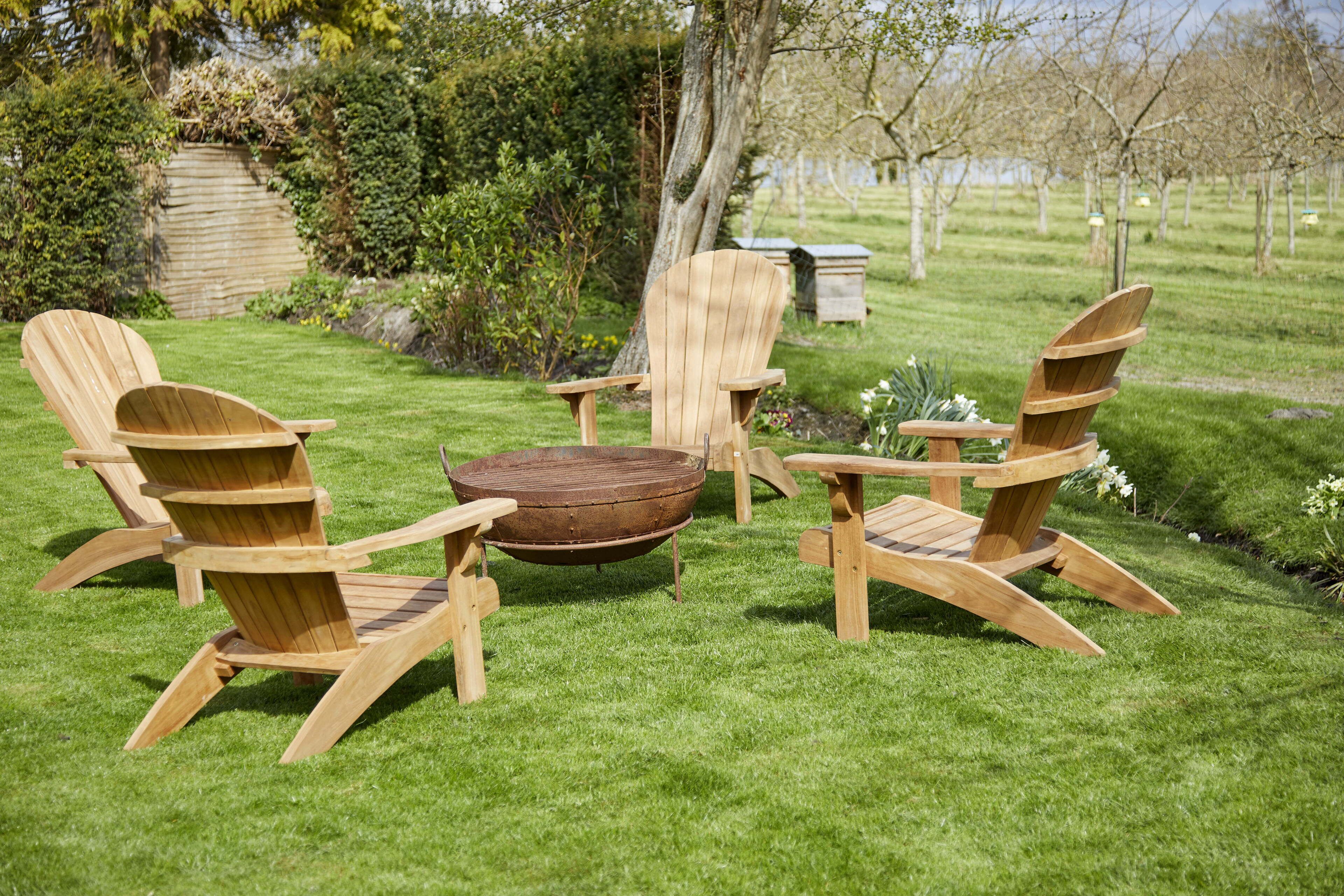 A set of wooden Adirondack chairs and a round wooden table in a grassy outdoor area.
