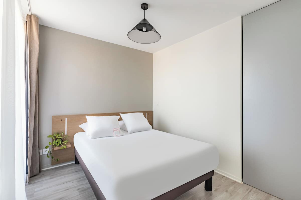 Ein modernes Hotelzimmer mit einem großen Bett, einem Holzkopfende, einer hängenden Pendelleuchte und einer kleinen Pflanze auf dem Nachttisch.