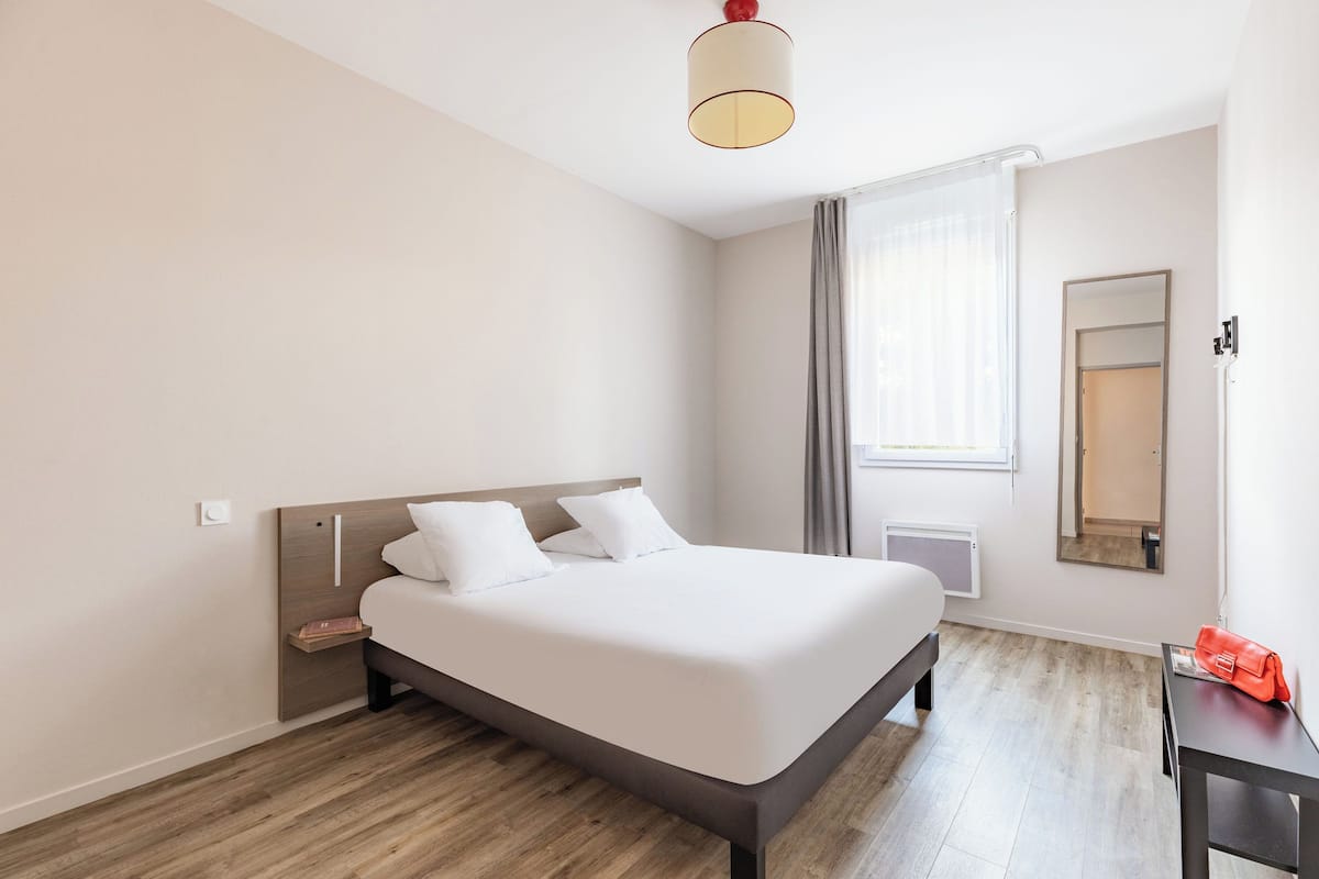 Ein modernes Hotelzimmer mit einem großen Bett, einem Nachttisch, einem Spiegel und einem Fenster mit Vorhängen.