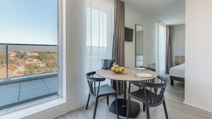 Une chambre d’hôtel moderne avec un balcon, une table de salle à manger ronde entourée de chaises, un lit et un téléviseur fixé au mur.