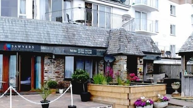 A building with a stone facade, a sign for 'SAWYERS' restaurant, and a small outdoor seating area with planters. - Sawyers Bed and Breakfast (Looe)