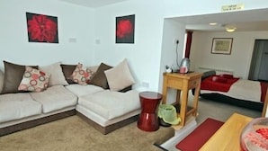 A modern living room with a sectional sofa, a small wooden table, and a red accent chair. - Sawyers Bed and Breakfast (Looe)