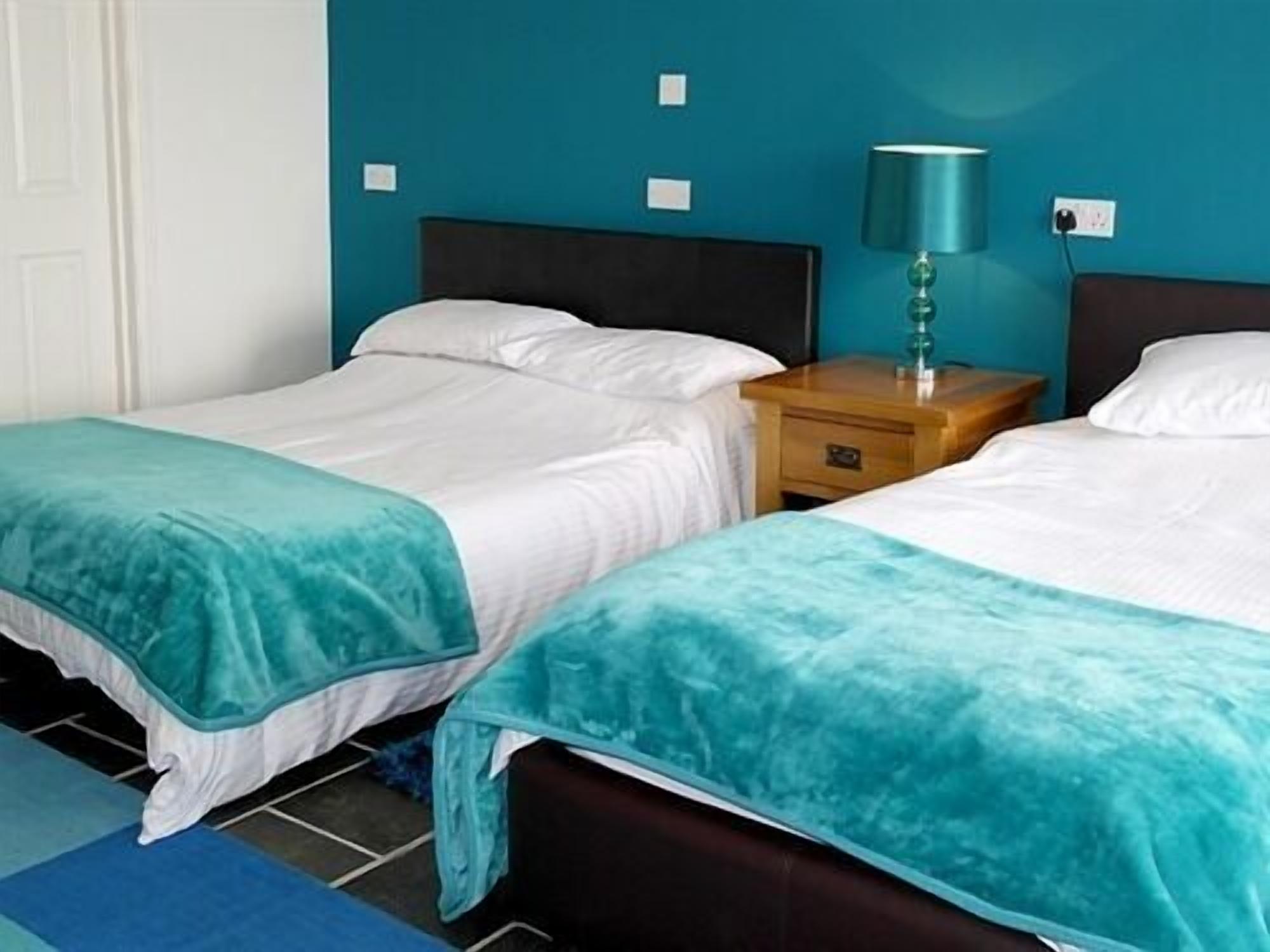 A hotel room with two single beds, a nightstand with a lamp, and teal-colored walls.