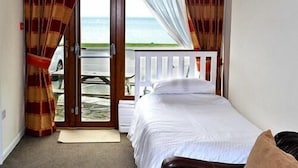 A bedroom with a bed, a view of the sea, and a door leading to a balcony. - Sawyers Bed and Breakfast (Looe)