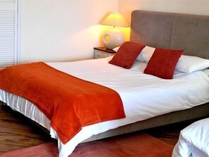 A neatly made bed with white and orange bedding, a grey headboard, and a bedside lamp. - Sawyers Bed and Breakfast (Looe)