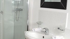 A bathroom with a glass shower enclosure, a white sink with a mirror above it, and a small shelf with toiletries. - Sawyers Bed and Breakfast (Looe)
