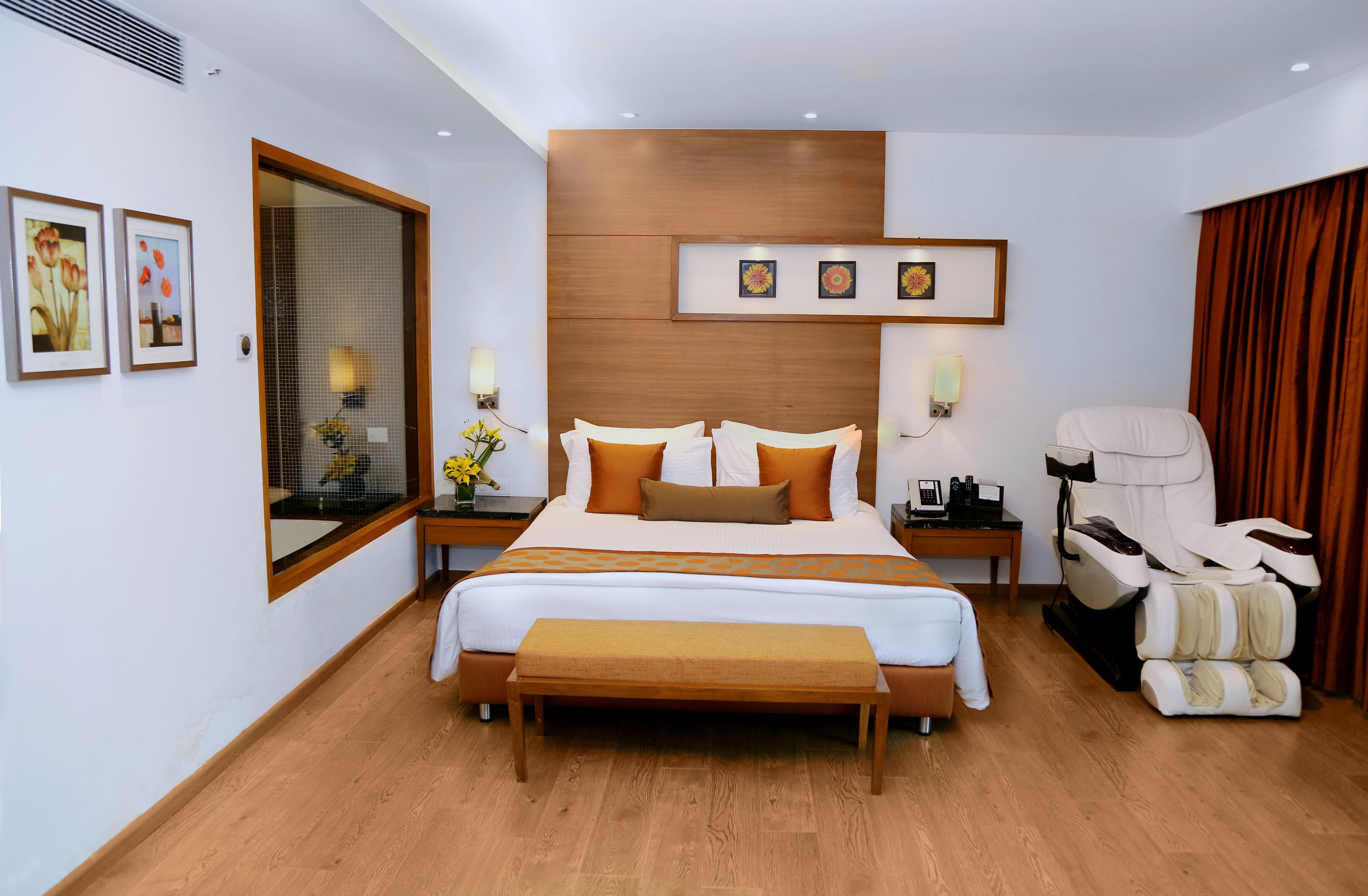 Quarto de hotel moderno com uma cama grande, poltrona de massagem e obras de arte nas paredes.
