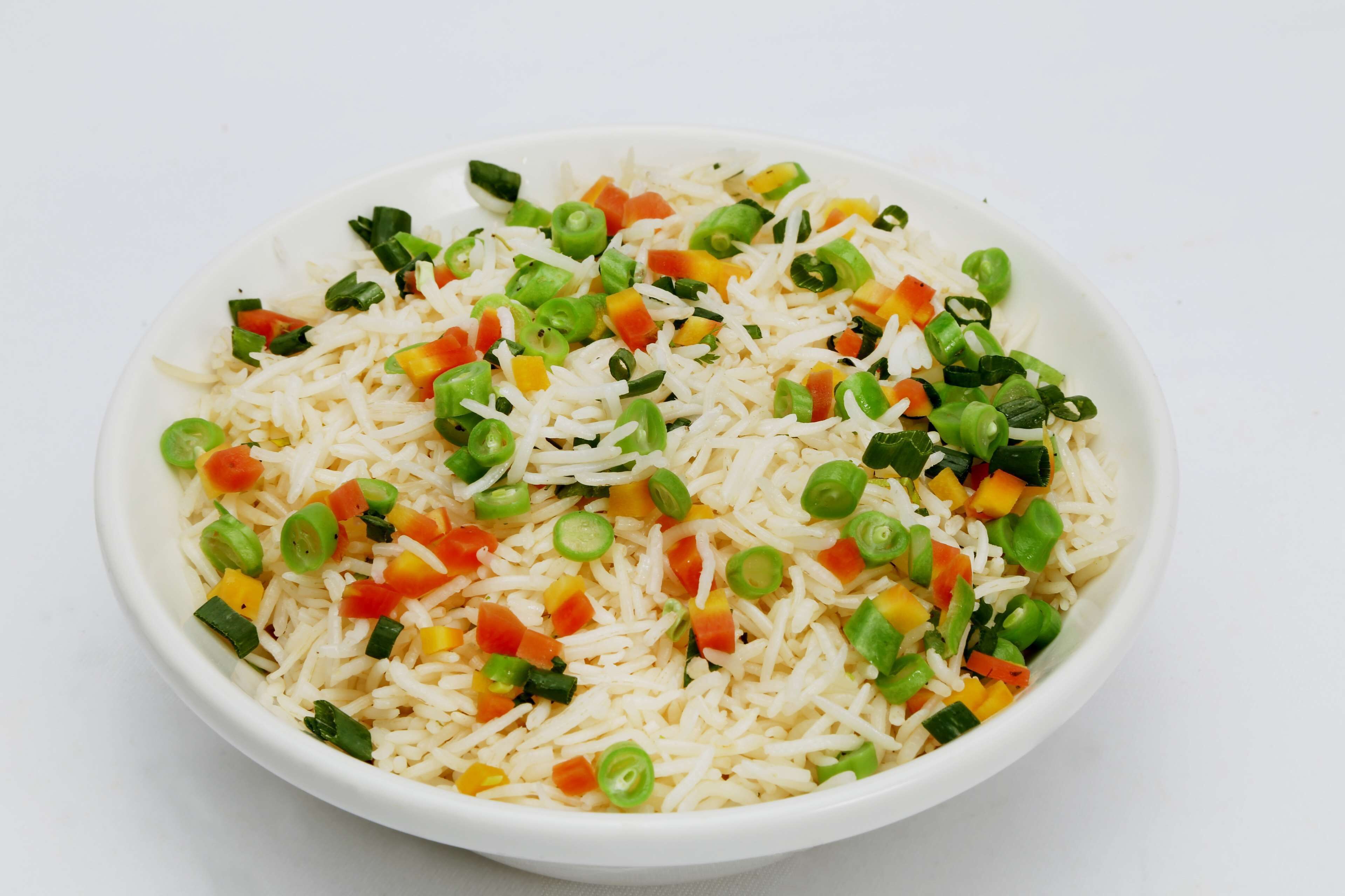 Un tazón de arroz mezclado con guisantes verdes, zanahorias picadas y cebollines.