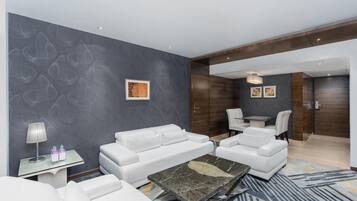A modern hotel room with a grey textured wall, white leather sofa, a marble coffee table, and a small side table with a lamp and bottles.