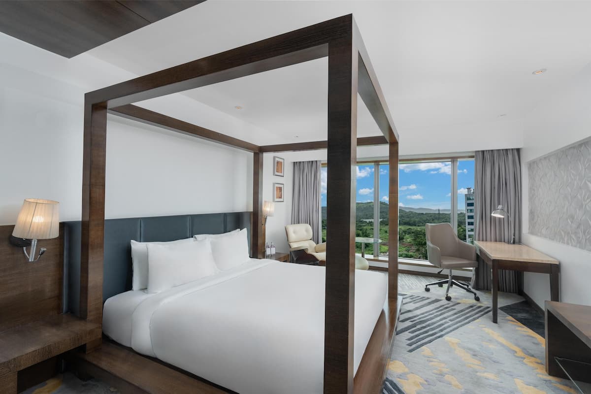 A hotel room with a large bed, a desk, a chair, and a view of the outdoors.
