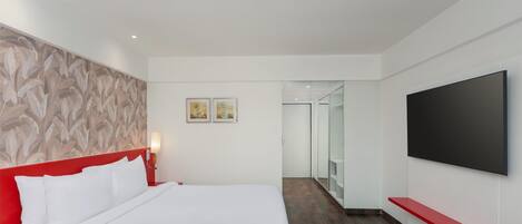 Habitación de hotel con una cama grande, cabecera roja, televisor de pantalla plana montado en la pared y piso de madera.