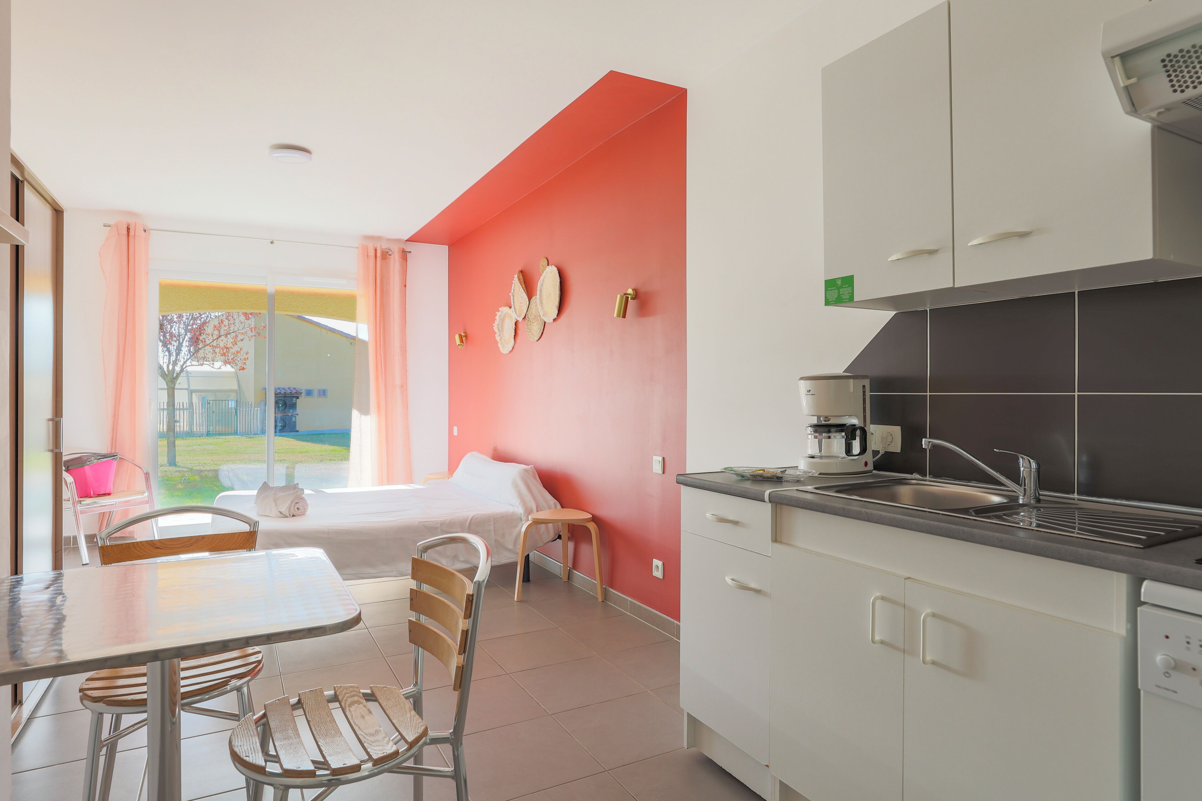 A modern kitchen with white cabinets, a coffee maker, and a sink. There is a dining area with a table and chairs.