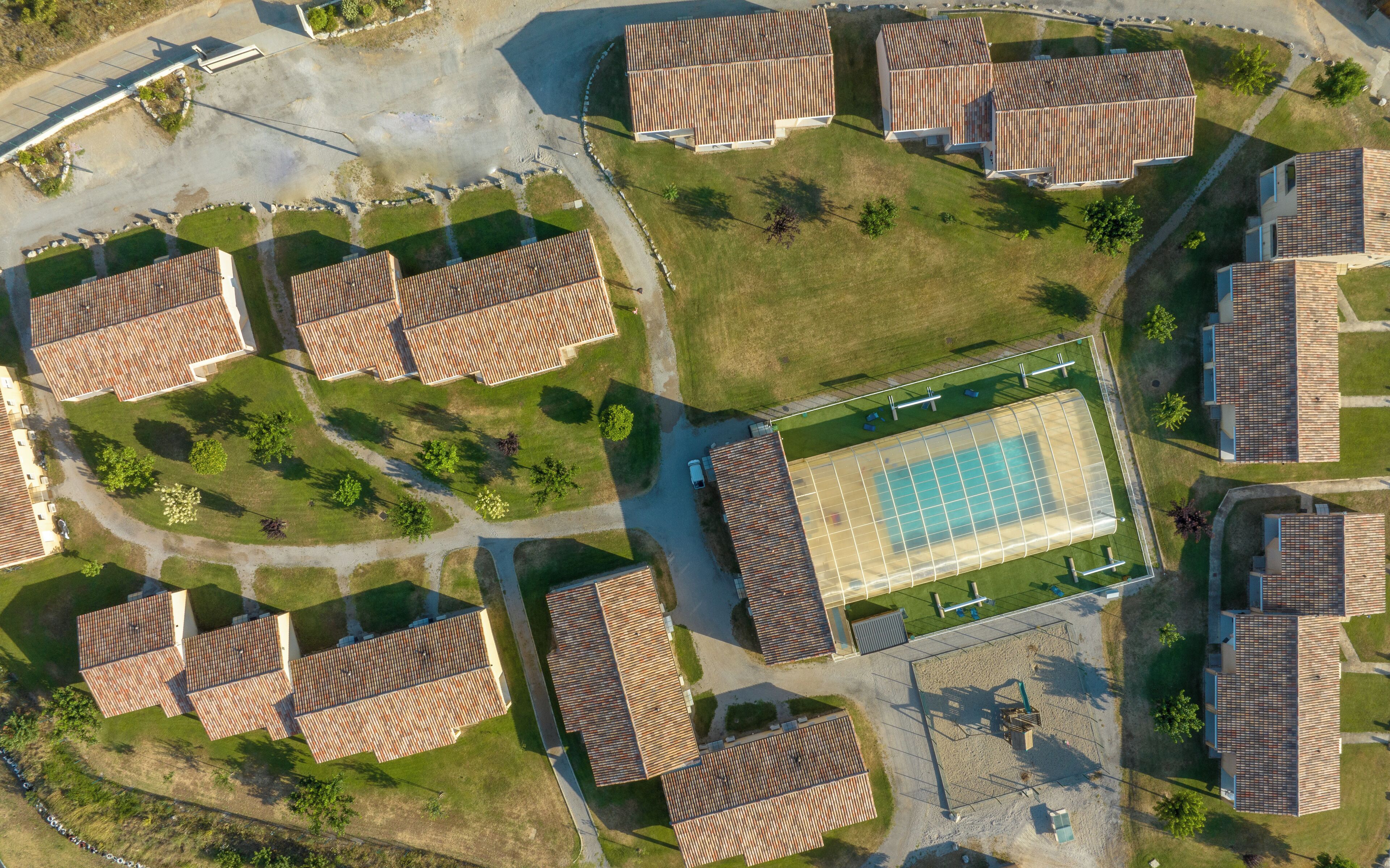 Vista aérea de una zona residencial con varias casas, una piscina central y áreas verdes circundantes.