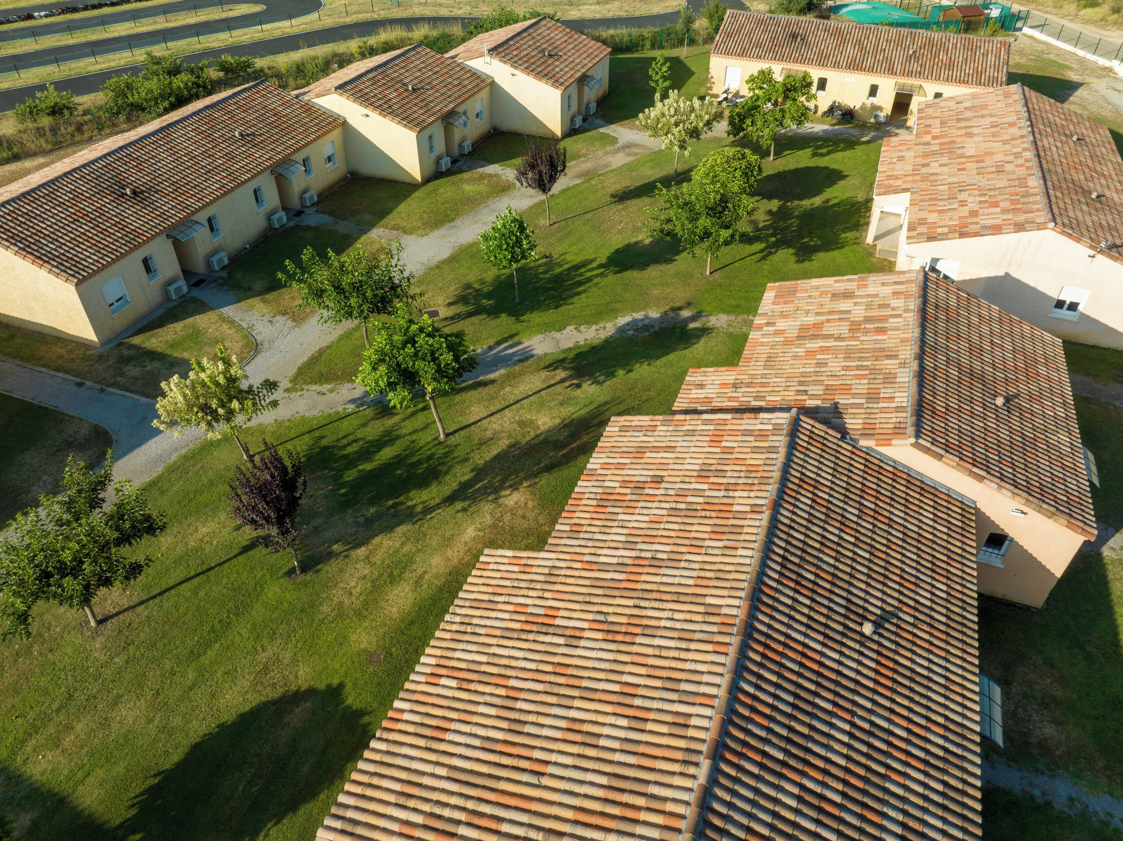 An aerial view of a residential area with multiple houses featuring tiled roofs and surrounded by green lawns and trees.