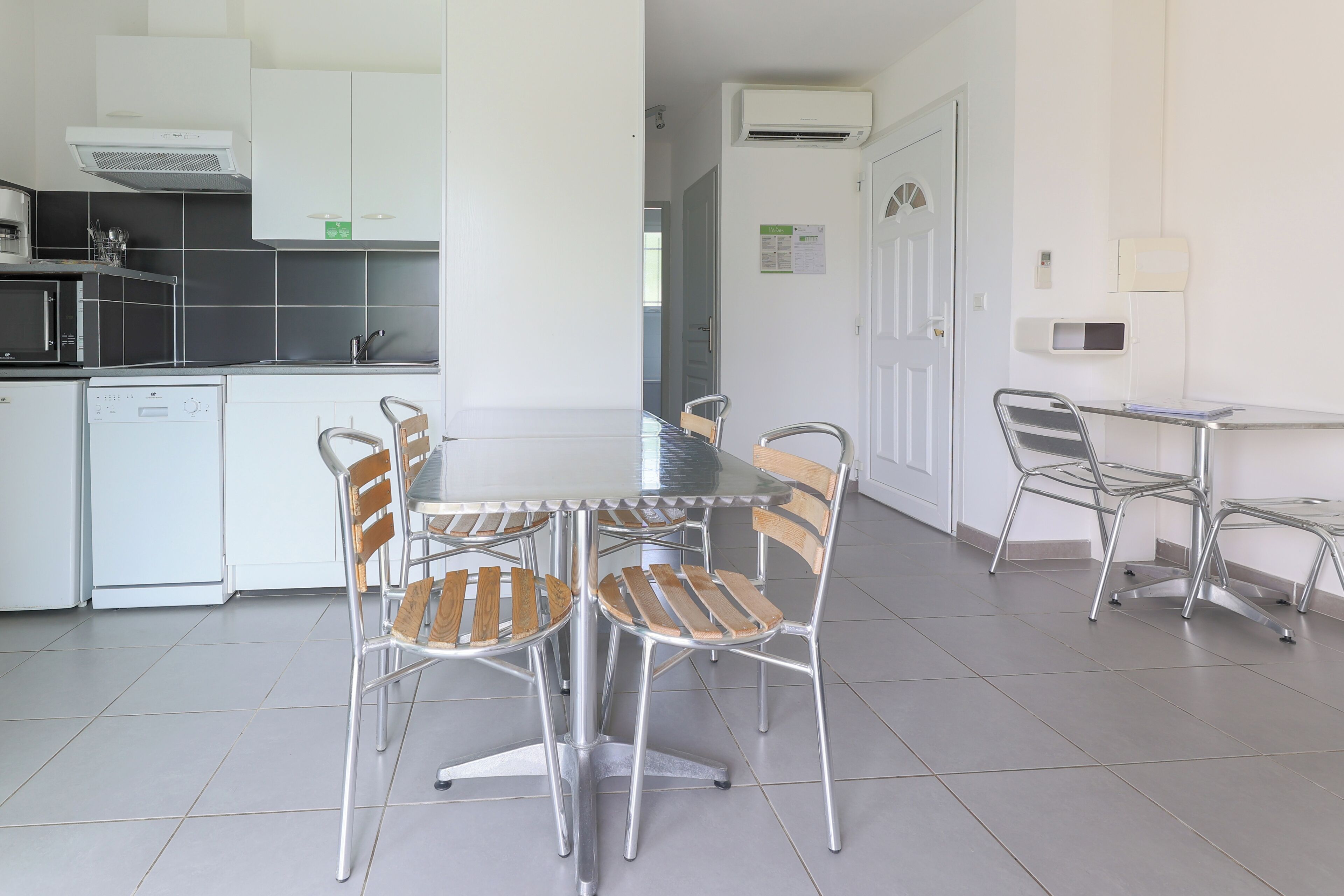 A modern kitchen with white cabinets, a built-in oven, and a dishwasher. There is a dining area with a table and chairs.