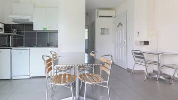 A modern kitchen with white cabinets, a built-in oven, and a dishwasher. There is a dining area with a table and chairs.
