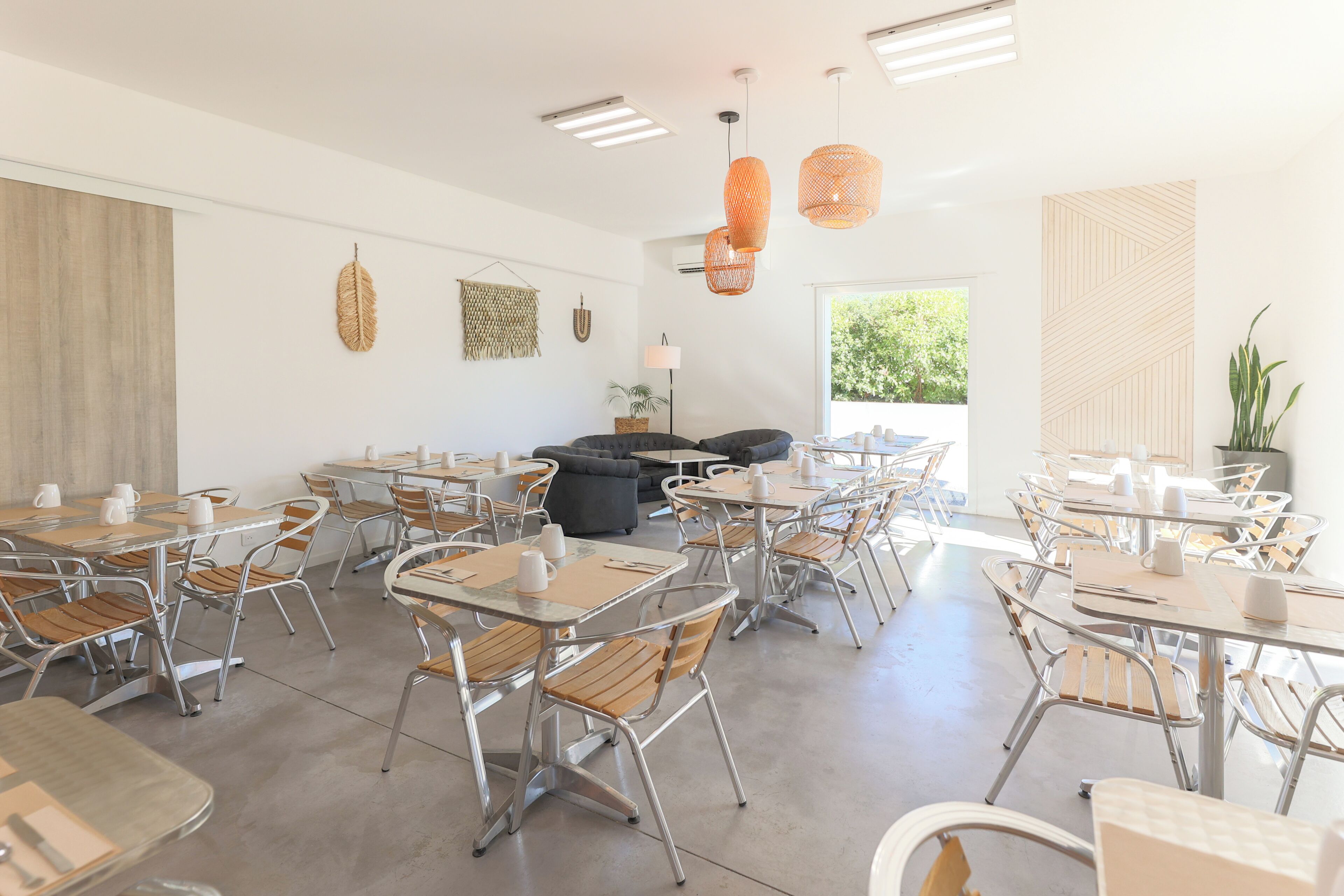 A modern cafe with round tables, metal chairs, and hanging orange pendant lights.