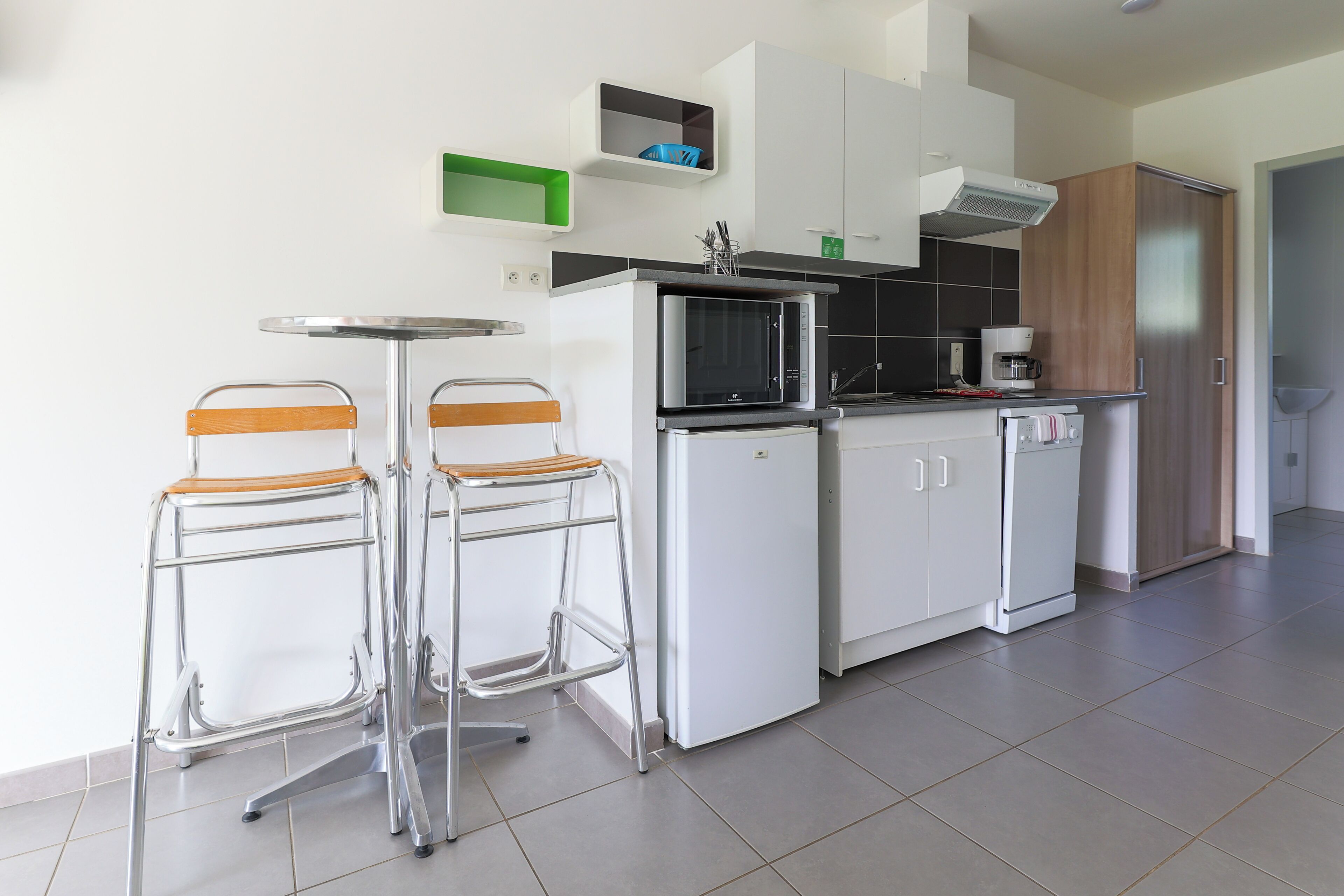 A modern kitchen with two bar stools, a microwave, a coffee maker, and cabinets.