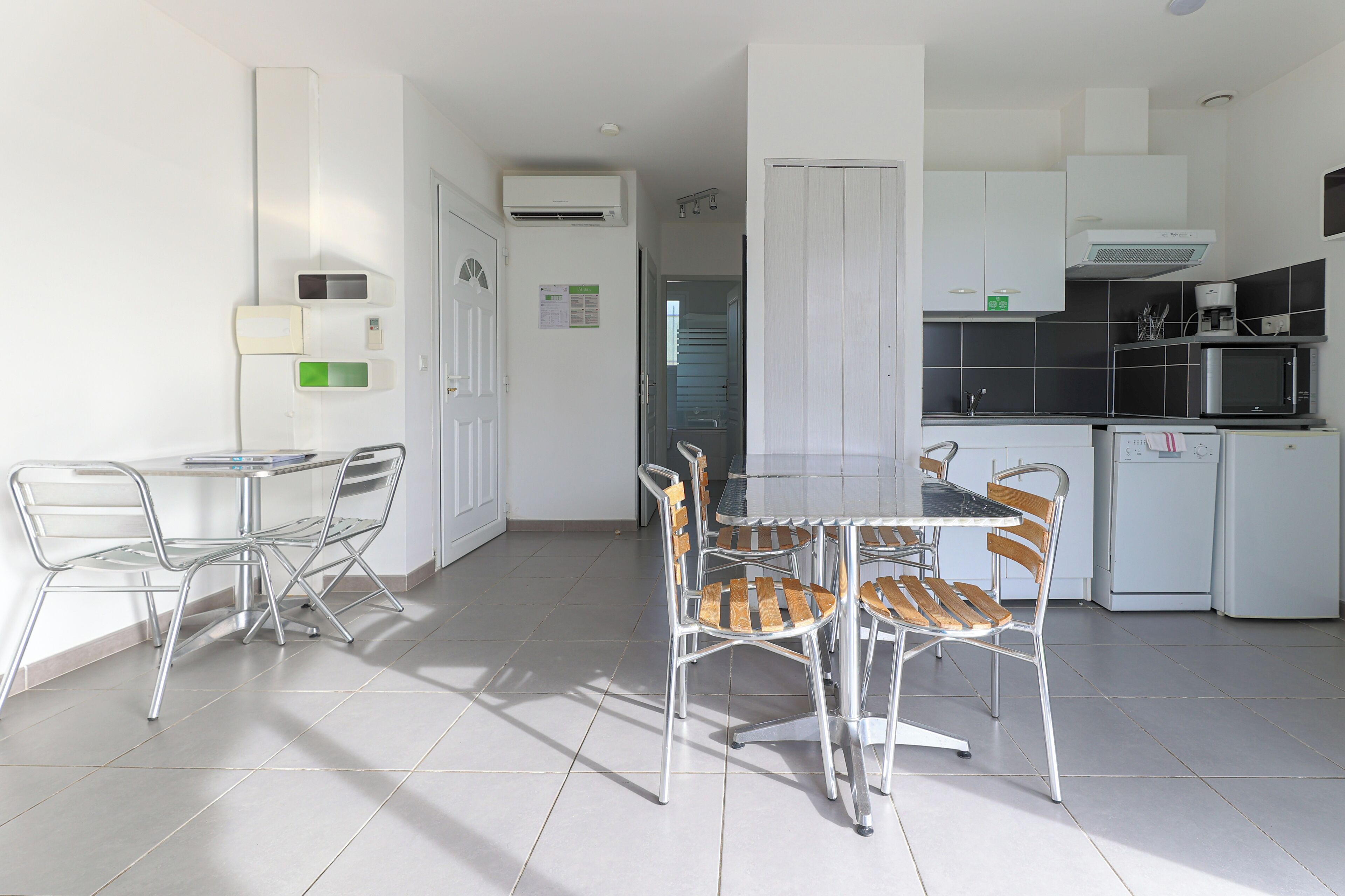Una cocina moderna con armarios blancos, un microondas y un refrigerador. Hay un comedor con una mesa y sillas.