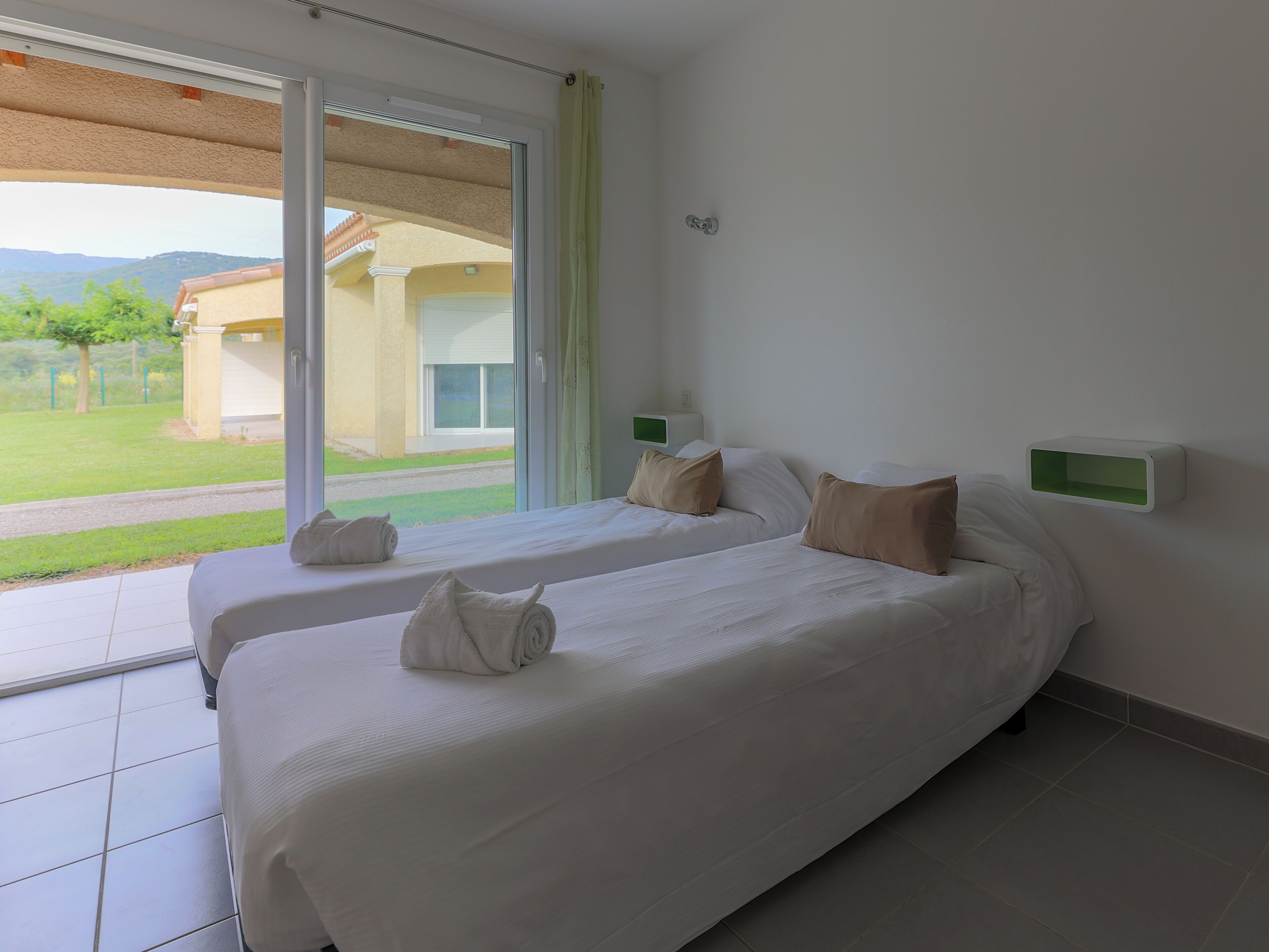 A hotel room with two beds, a sliding glass door to the outside, and a small green-framed wall-mounted shelf.
