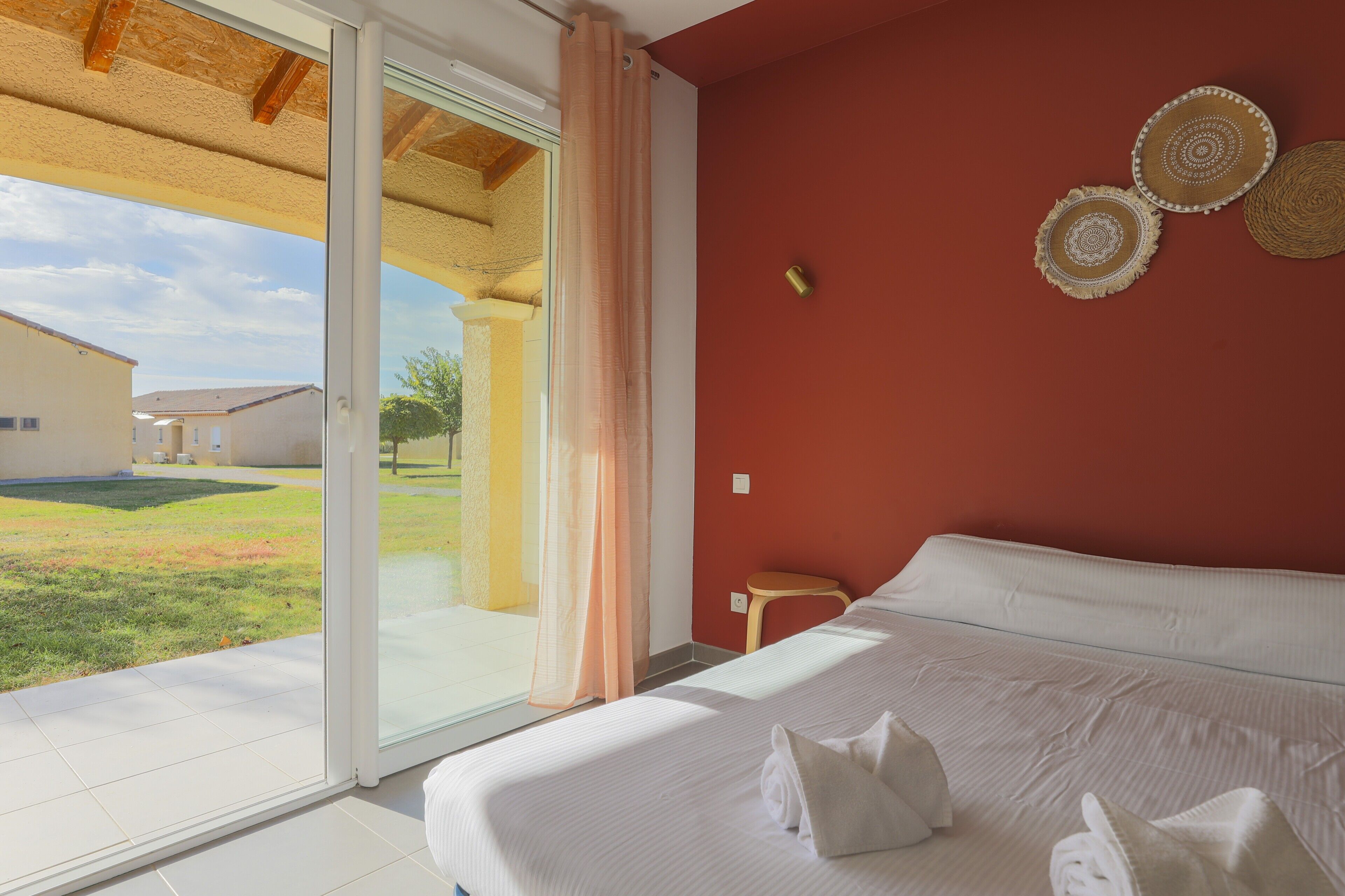 Une chambre d’hôtel avec un grand lit, une porte-fenêtre coulissante donnant sur l’extérieur et un petit tabouret en bois.