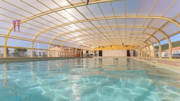 An indoor swimming pool with a curved glass ceiling and purple pennant flags. - Résidence du Parc - Gorges de l'Hérault - Cévennes - Parc Sports & Loisirs Brissac Ganges (Brissac)