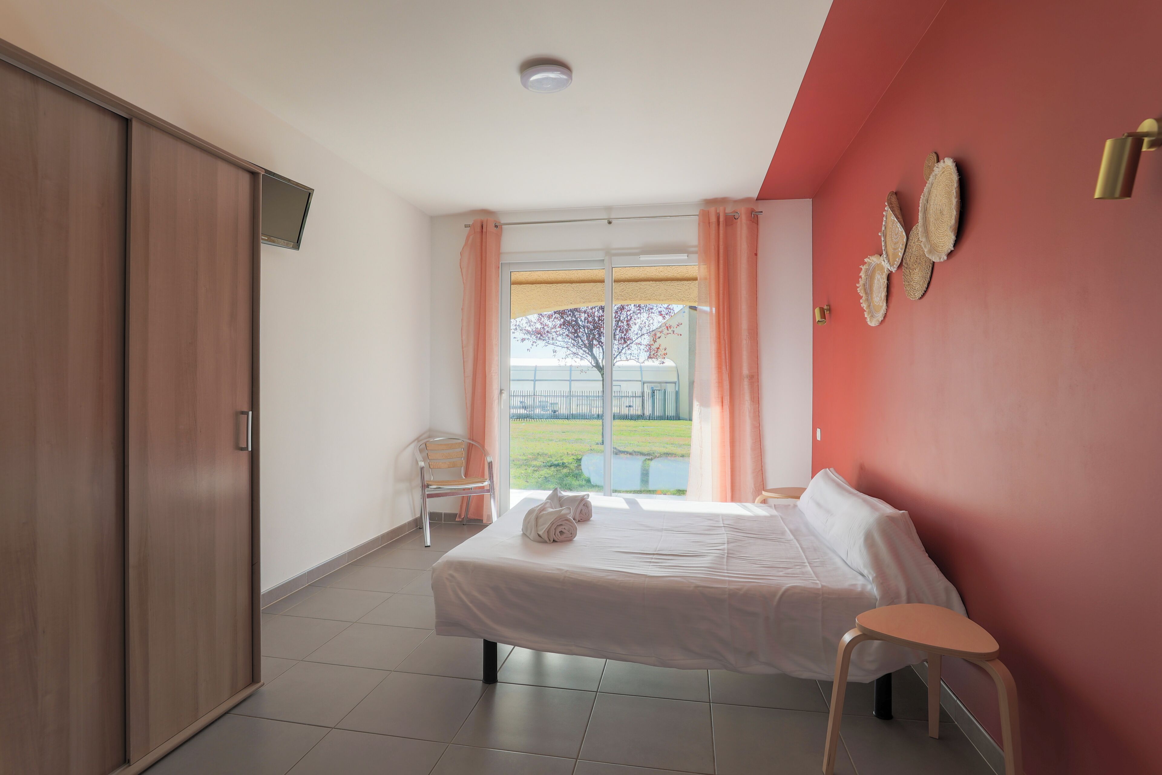 A hotel room with a bed, a chair, a wardrobe, and a window with curtains.