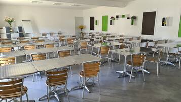 A spacious classroom with rows of tables and chairs, a whiteboard, and green accents on the walls.