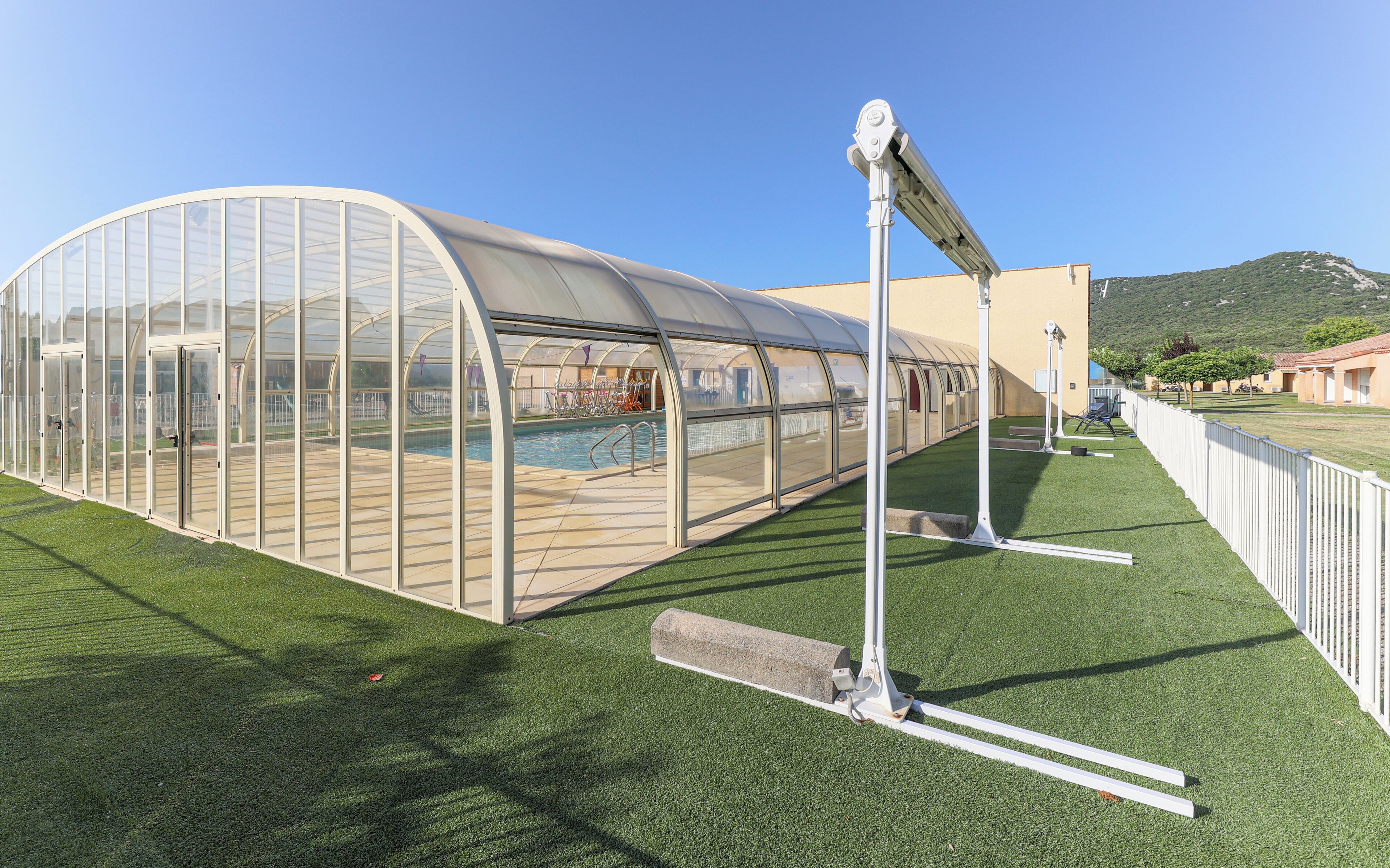 A greenhouse structure with a transparent roof, a pool, and artificial grass.