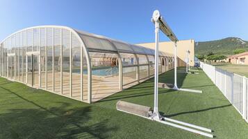 A greenhouse structure with a transparent roof, a pool, and artificial grass.