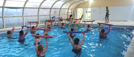 Une piscine intérieure dotée d’un toit en verre incurvé, de plusieurs couloirs et de nageurs utilisant des dispositifs flottants.