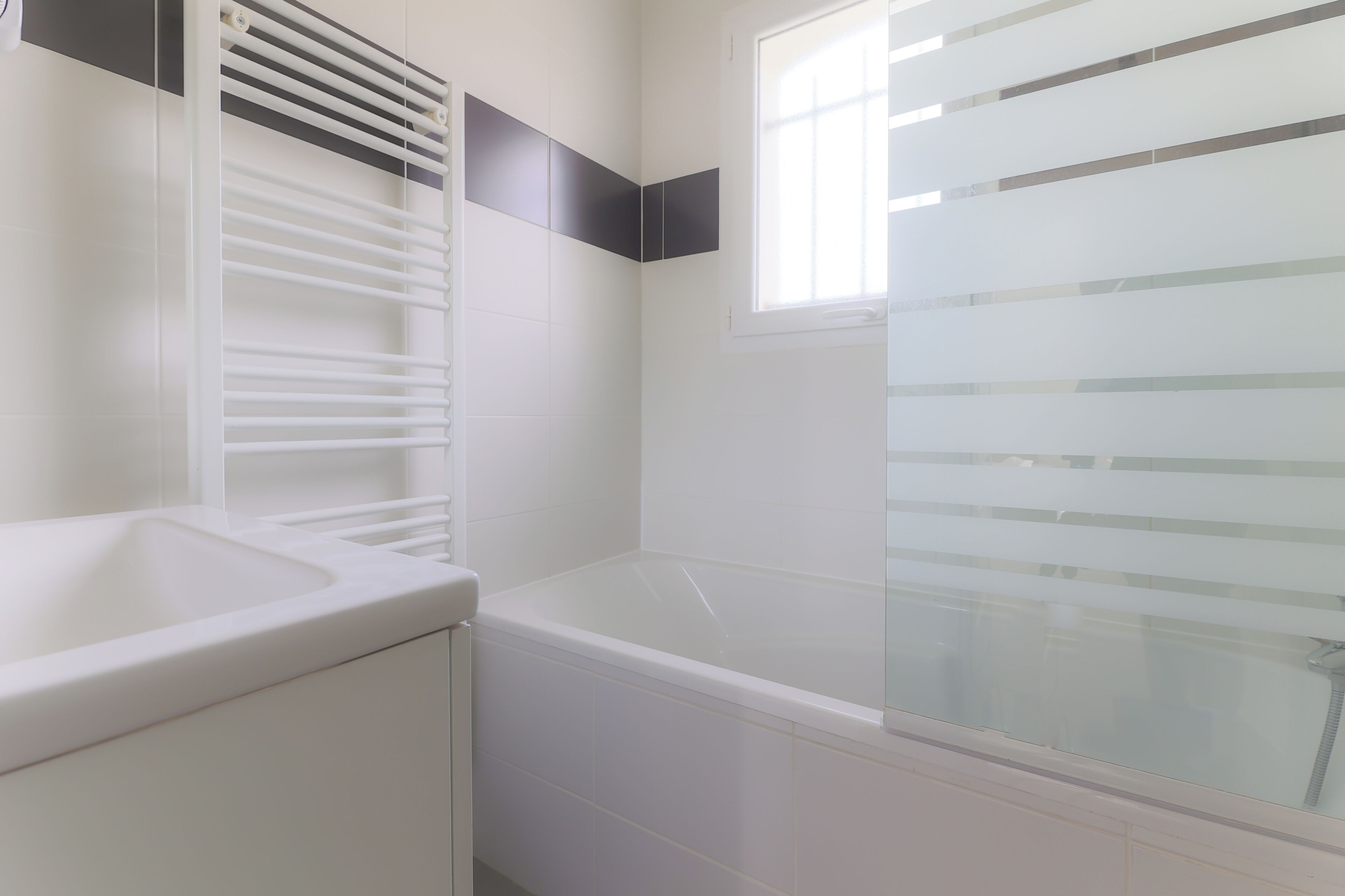 Ein Badezimmer mit Badewanne, Toilette und Waschbecken. Ein Fenster mit Jalousien ist vorhanden.