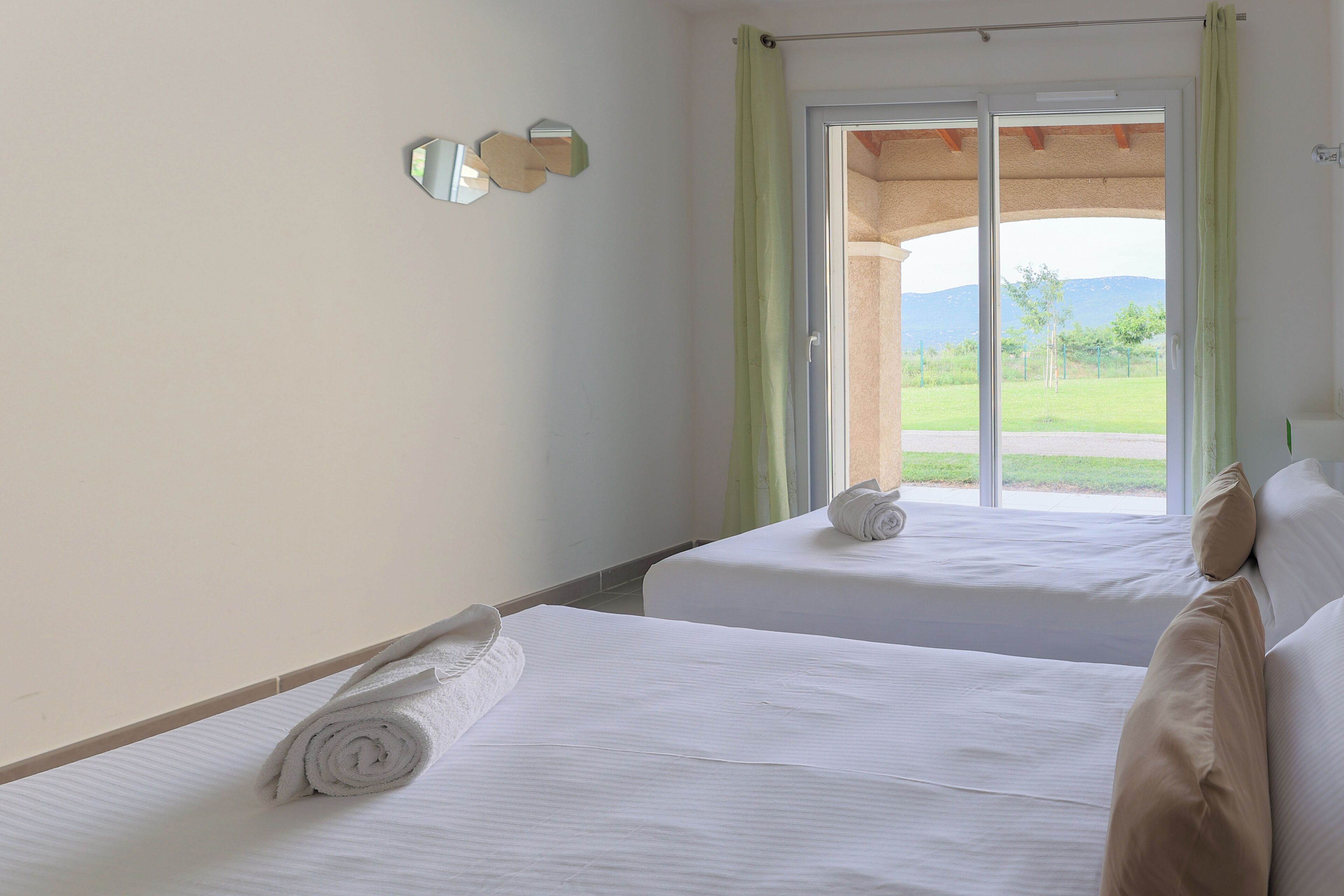 A hotel room with two beds, a window with a view of a garden, and a mirror on the wall.