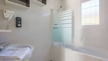 Un baño con lavamanos, secador de pelo, cabina de ducha de vidrio y ventana.