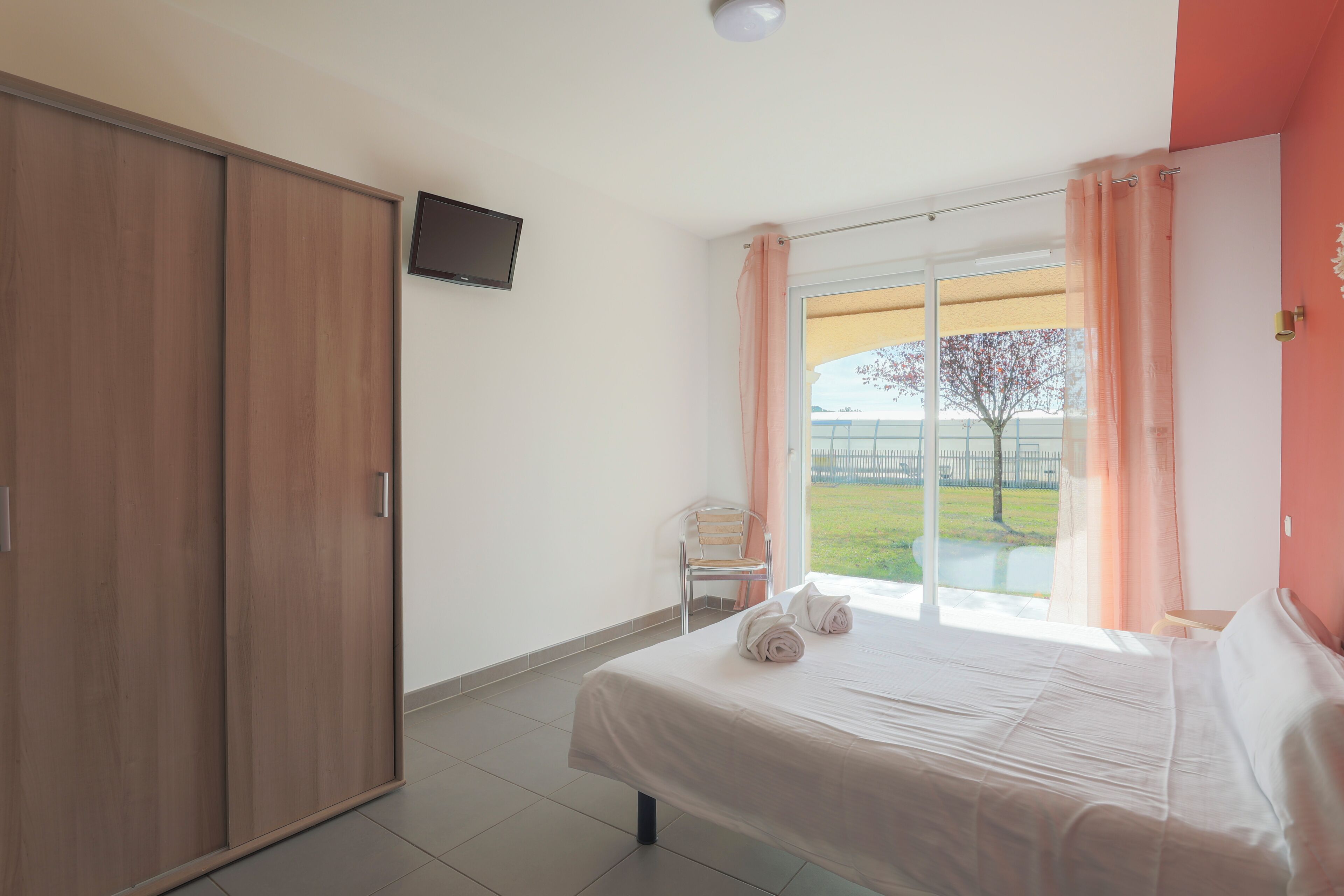 Un dormitorio con cama, televisión, puerta corredera y vistas al exterior.