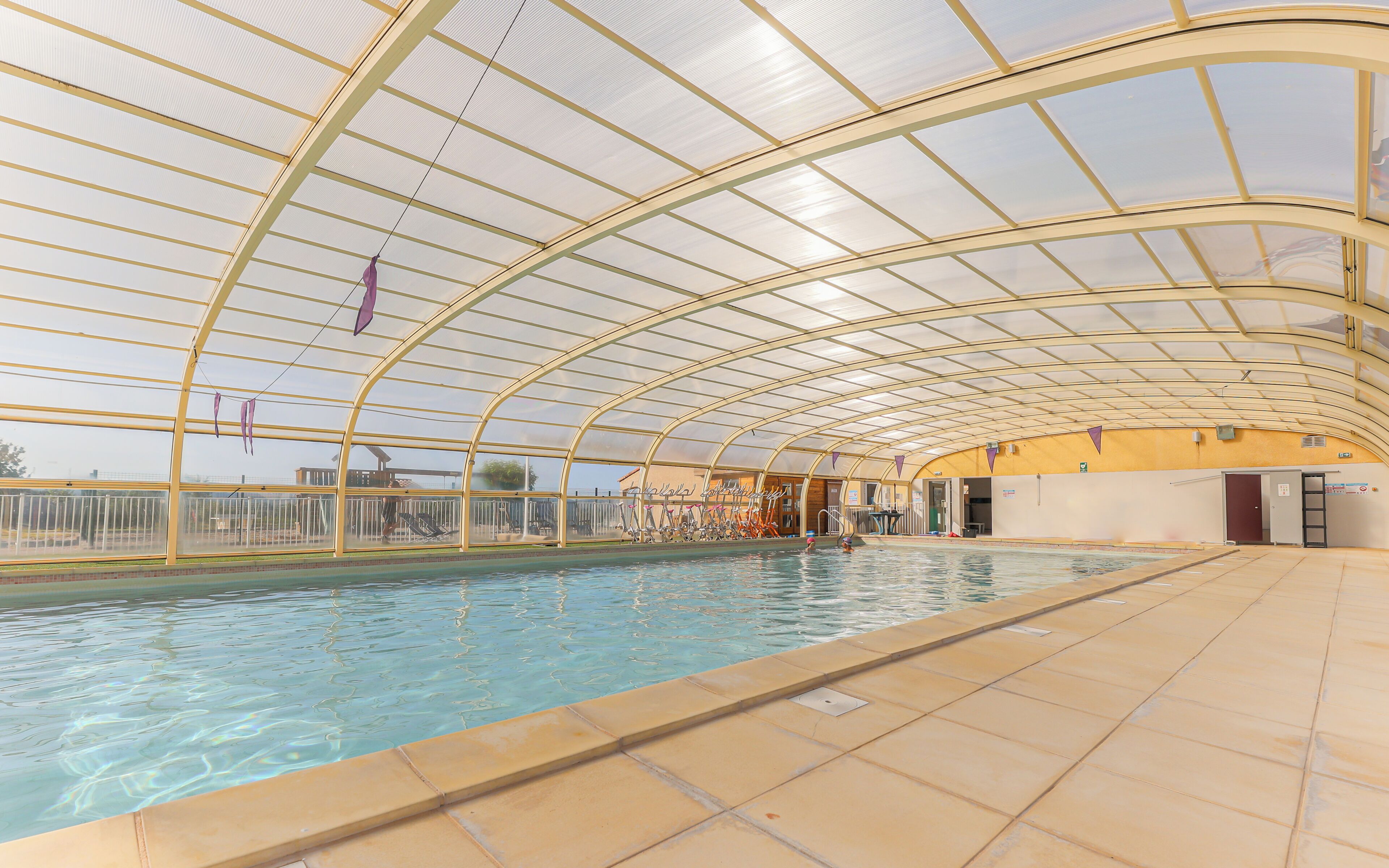 Une piscine intérieure dotée d’un toit en verre et d’un sol carrelé.