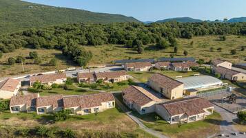A residential area with multiple houses featuring red-tiled roofs, surrounded by green hills and trees.