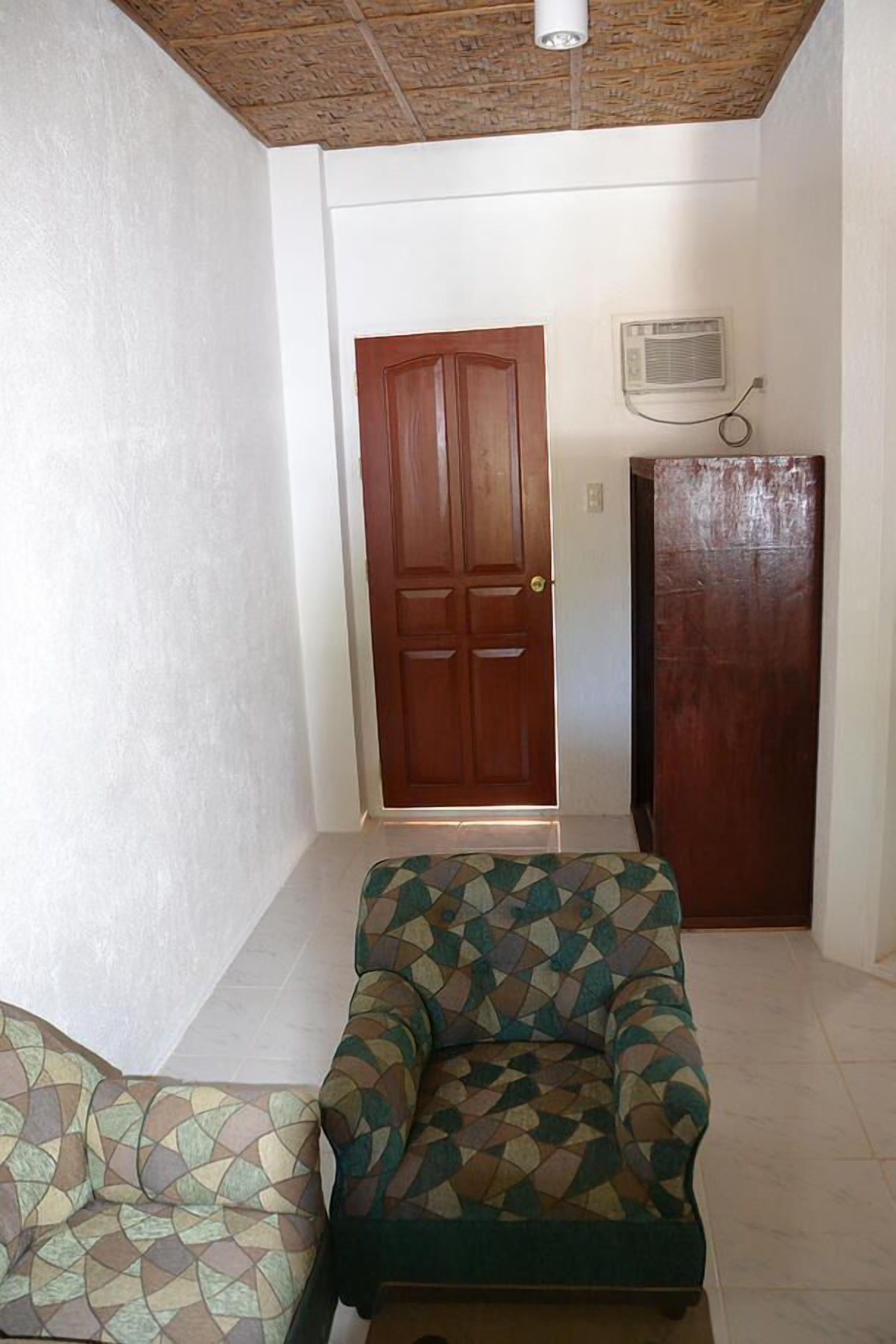 A room with a patterned sofa, a wooden door, and an air conditioning unit on the wall.