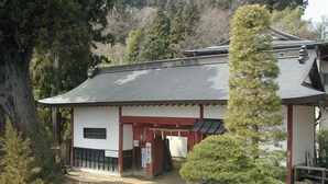 Un edificio japonés tradicional con tejado de tejas, estructura de madera y un pequeño jardín con un pino.