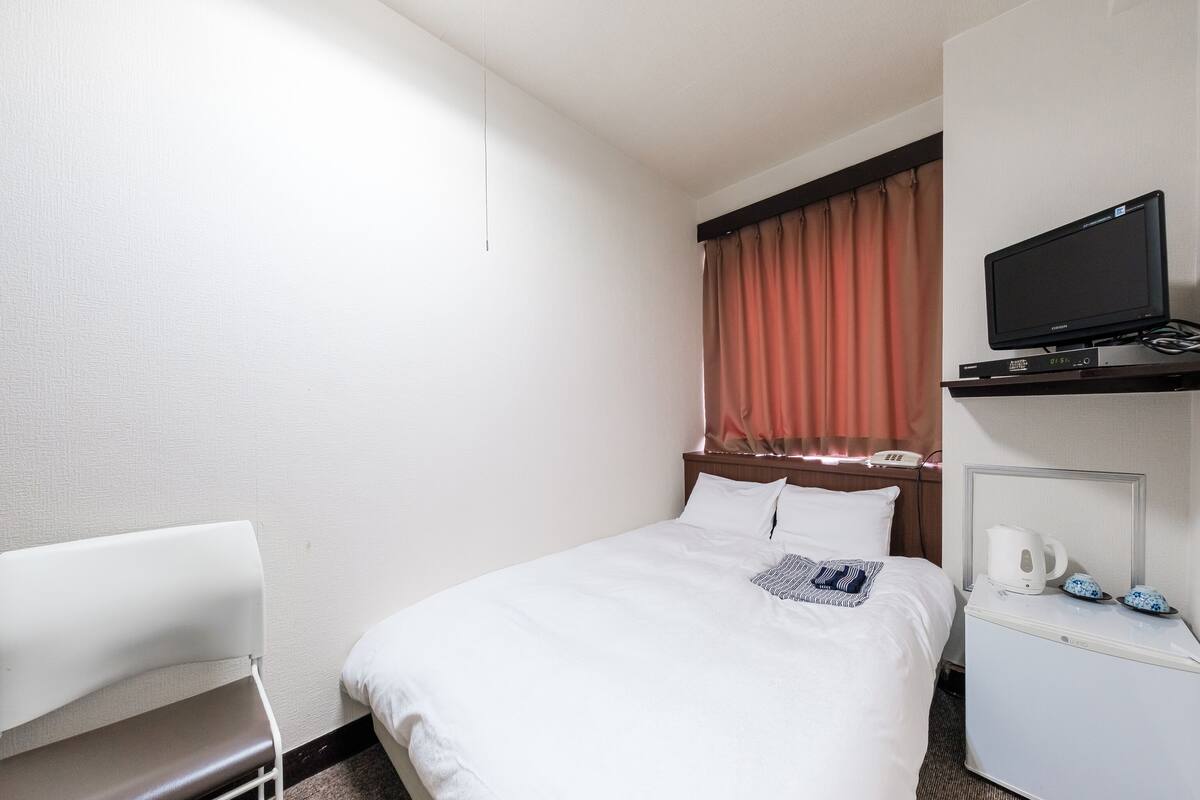 Une chambre d’hôtel avec un lit, un téléviseur posé sur une étagère, une chaise et une machine à café.