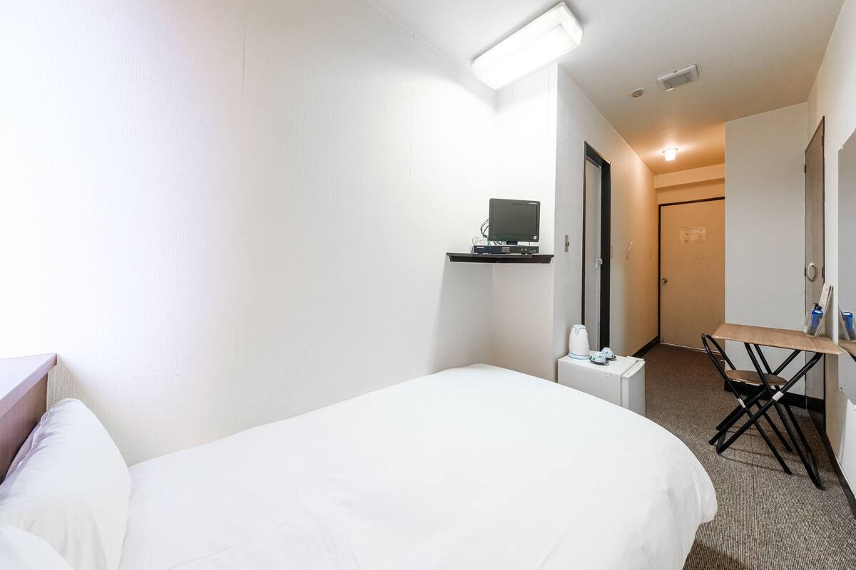 Une chambre d’hôtel comprenant un lit, un bureau avec un ordinateur, une chaise et une petite table avec une bouilloire.