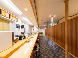 Interior de un restaurante con una barra larga, paneles de madera en una pared y suelo de baldosas.